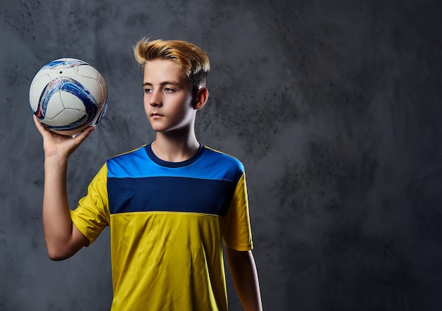 Retrato de adolescente loiro, jogador de futebol vestido com um uniforme amarelo detém uma bola.