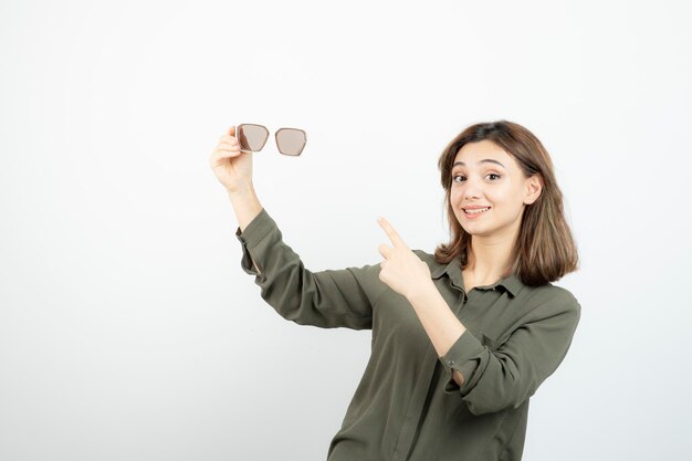 Retrato de adorável jovem apontando para óculos sobre branco. Foto de alta qualidade