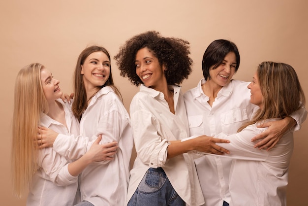 Foto grátis retrato de adultos multiétnicos e mulheres jovens em camisas brancas, abraçando-se em fundo marrom