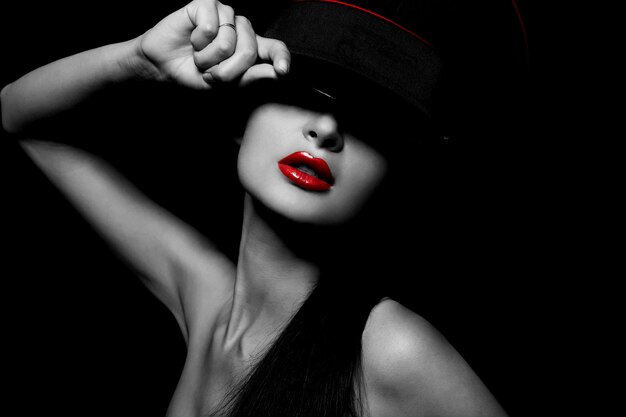 Retrato de alta moda look.glamour da bela jovem fêmea sexy com lábios vermelhos em fundo preto com chapéu
