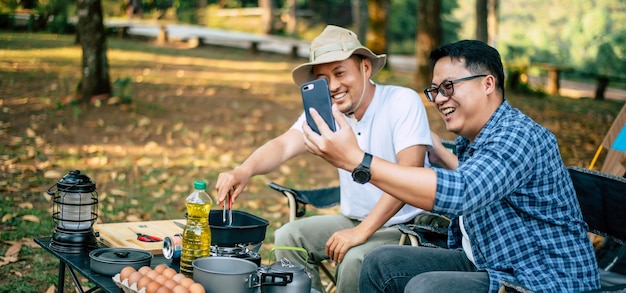 Retrato de amigos asiáticos felizes fazendo uma chamada de vídeo com smartphone no acampamento cozinhando em frente ao chão cozinhar ao ar livre viajando acampamento conceito de estilo de vida