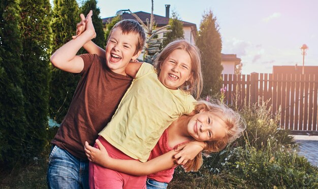 Retrato de amiguinhos felizes se divertindo no quintal. Três amiguinhos fofos abraçando e brincando.