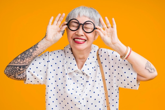 Foto grátis retrato de atraente tatuagem asiática funky alegre grisalha idosa idosa tocando óculos isolados sobre cores de fundo amarelo pastel surpresa e sobre a expressão de sentimento de saída