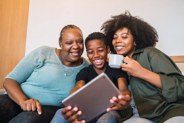 Retrato de avó afro-americana, mãe e filho tirando uma selfie com tablet digital em casa.