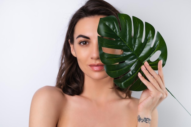 Retrato de beleza aproximado de uma mulher em topless com pele perfeita e maquiagem natural com folha de palmeira monstera