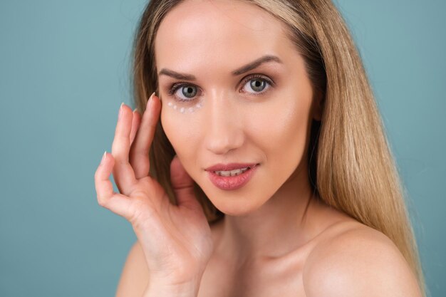 Retrato de beleza de close-up de uma mulher de topless com pele perfeita e maquiagem natural, com pontos de creme antienvelhecimento para hidratar e firmar a pele sob os olhos