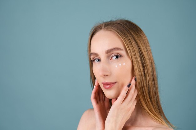 Retrato de beleza de close-up de uma mulher de topless com pele perfeita e maquiagem natural, com pontos de creme antienvelhecimento para hidratar e firmar a pele sob os olhos