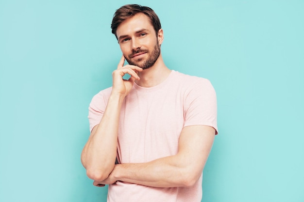 Retrato de bonito sorridente elegante hipster lambersexual modelo Homem sexy vestido de camiseta rosa e calças Moda masculina isolada na parede azul no estúdio