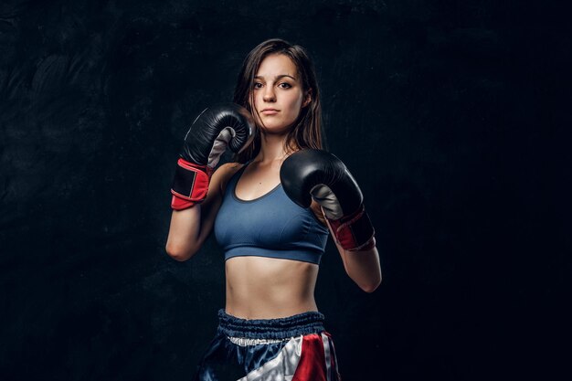 Retrato de boxeador feminino sério em luvas de boxe e desgaste esportivo no estúdio fotográfico escuro.