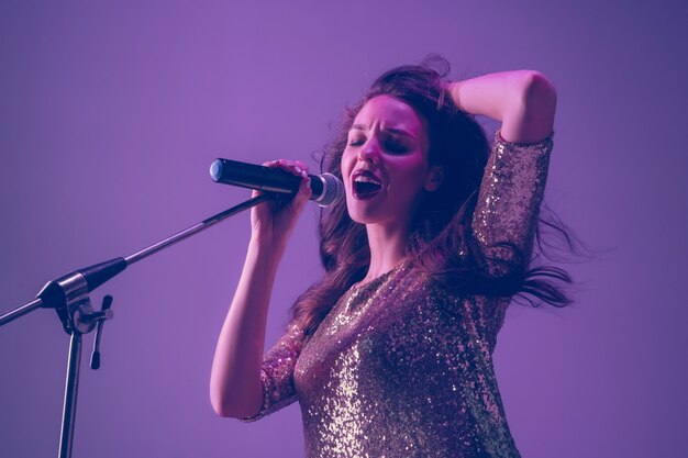 Retrato de cantora caucasiana isolado em estúdio roxo em luz de néon