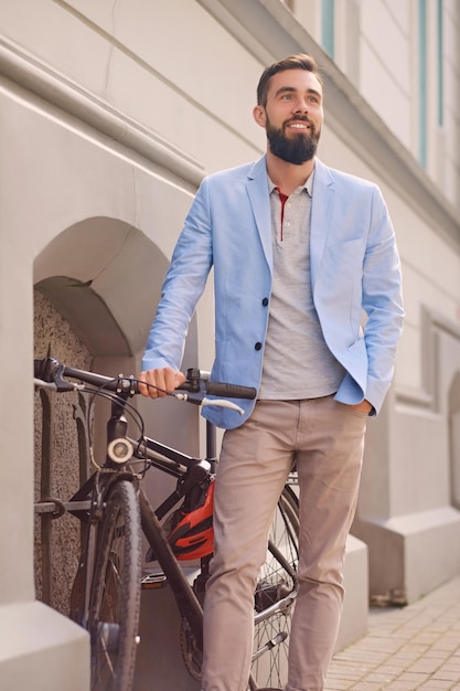 Retrato de cara barbudo elegante perto da bicicleta retrô em uma cidade velha.