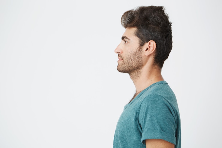 Foto grátis retrato de cara metade do belo homem espanhol, em casual camiseta azul, com barba e cabelo da moda, mostrando o seu perfil e olhando para a esquerda. copie o espaço.