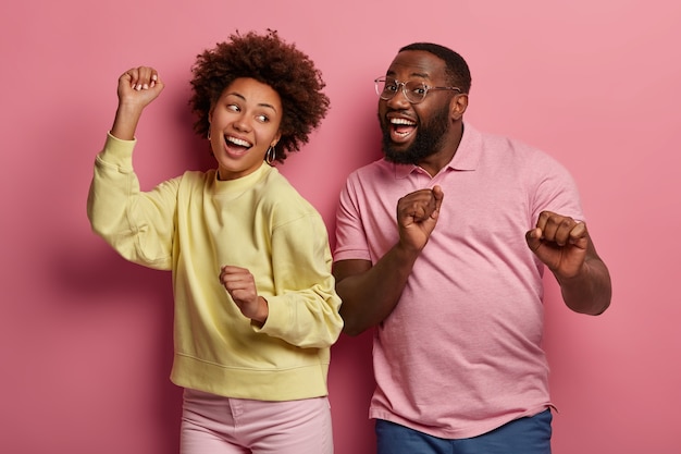 Retrato de casal energizado de pele escura dança feliz, inspirou expressões faciais alegres, sorri amplamente, move-se com música