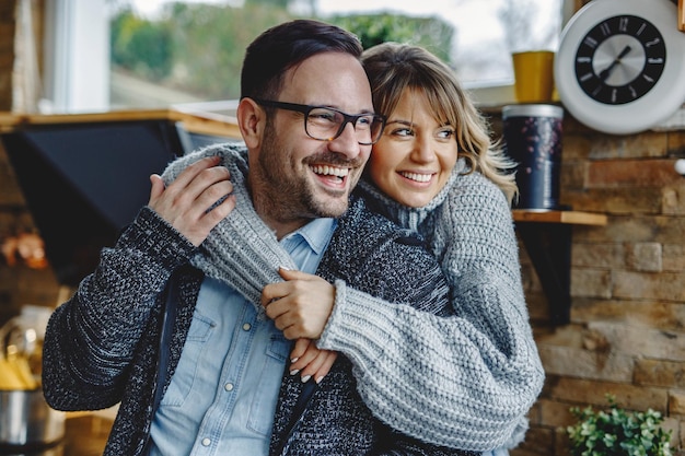 Retrato de casal feliz apaixonado, abraçando na cozinha e olhando para longe