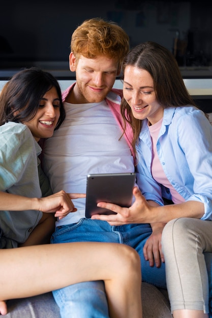 Foto grátis retrato de casal poliamoroso em casa sentado no sofá e usando tablet