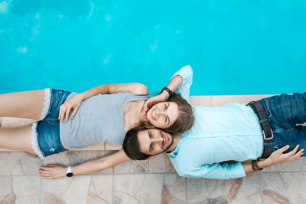 Retrato de casal sorridente deitado vestido perto da piscina. eles se adoram