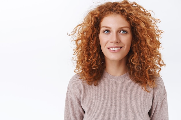 Foto grátis retrato de close-up atraente, feminina, adorável ruiva mulher com cabelo natural encaracolado, usar blusa bege, sorrindo com uma expressão encantada e entusiástica, parede branca de pé divertida