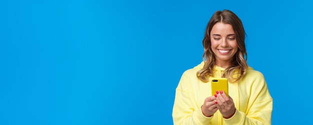 Retrato de close-up boba linda mulher europeia loira com capuz amarelo sorrindo para o telefone celular