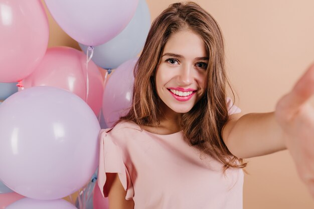 Retrato de close-up da alegre modelo feminina branca com maquiagem brilhante, aproveitando a festa de aniversário