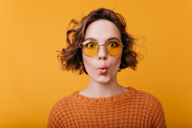 Retrato de close-up de menina bonita isolada em um espaço amarelo com expressão de rosto se beijando