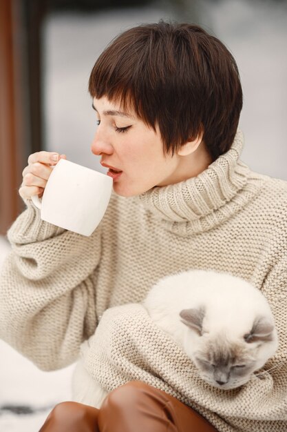 Retrato de close-up de mulher em suéter branco com gato branco, bebendo chá