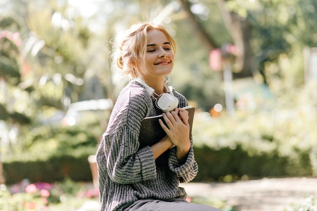 Retrato de close-up de mulher sentada em uma estufa com fones de ouvido e livro