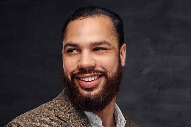 Retrato de close-up de um empresário afro-americano barbudo bonito sorridente em uma jaqueta clássica marrom. Isolado em um fundo escuro.