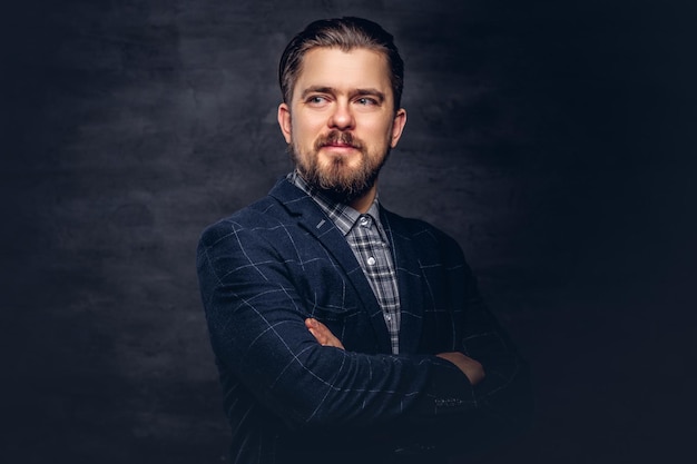 Retrato de close-up de um homem de meia idade com barba e penteado vestido com um elegante terno azul em um fundo escuro texturizado no estúdio.