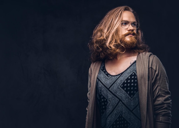 Foto grátis retrato de close-up de um homem ruiva hipster com cabelos longos e exuberantes e barba cheia, vestido com roupas casuais em pé em um estúdio, olhando para longe. isolado em um fundo escuro.