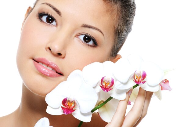 Retrato de close-up de uma bela garota asiática com uma flor perto do rosto - tratamento para a pele