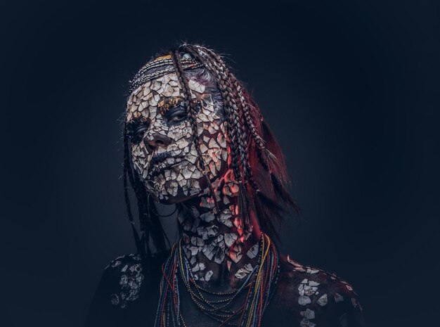 Retrato de close-up de uma bruxa da tribo indígena africana, vestindo traje tradicional. Conceito de maquiagem. Isolado em um fundo escuro.