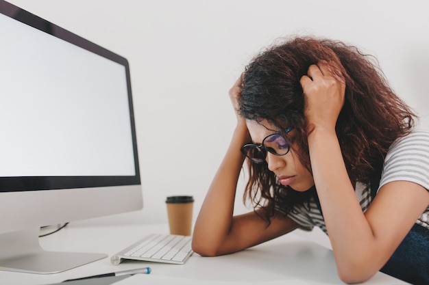 Foto grátis retrato de close-up de uma jovem triste perto do computador com uma tela branca e uma xícara de café