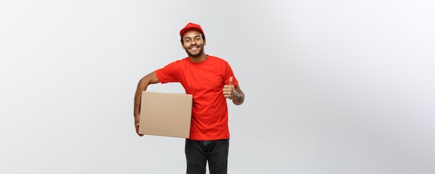 Retrato de conceito de entrega de entregador afro-americano feliz segurando um pacote de caixa e mostrando batidas isoladas no espaço de cópia de fundo do estúdio cinza