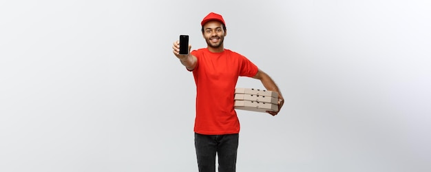 Retrato de conceito de entrega de entregador ou mensageiro afro-americano bonito com caixa de pizza mostrando o celular em você para verificar o pedido isolado no espaço de cópia de fundo do estúdio cinza