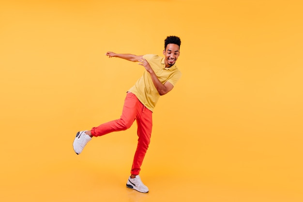 Retrato de corpo inteiro da alegre modelo masculino africano dançando com sapatos amarelos. Homem negro alegre desfrutando.