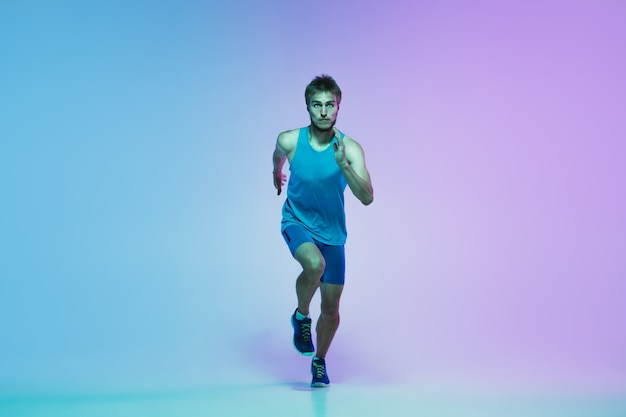 Retrato de corpo inteiro de ativo jovem caucasiano correndo, correndo homem no estúdio gradiente na luz de neon