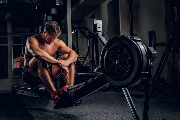 Retrato de corpo inteiro de homem desportivo cansado após treinos na máquina de exercício de força em um clube de ginástica.