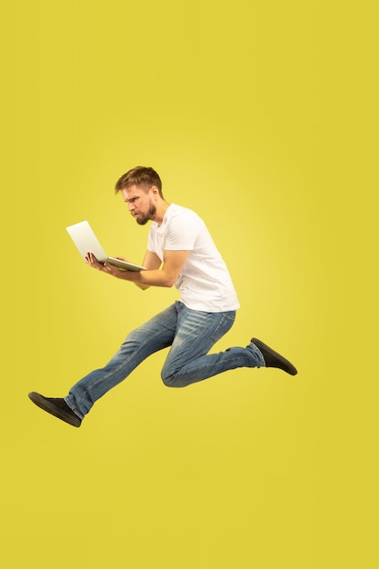 Retrato de corpo inteiro de homem pulando feliz isolado em fundo amarelo. modelo masculino caucasiano com roupas casuais