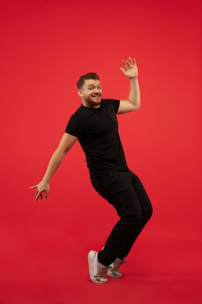 Retrato de corpo inteiro de jovem salto em altura isolado na parede vermelha. Modelo masculino caucasiano. Copyspace. Emoções humanas, expressão facial, conceito de esporte.