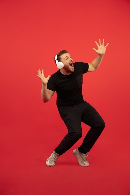 Retrato de corpo inteiro de jovem salto em altura isolado na parede vermelha. modelo masculino caucasiano. copyspace. emoções humanas, expressão facial, conceito de esporte.