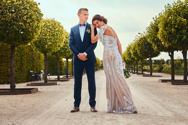 Retrato de corpo inteiro de recém-casados posando no belo jardim.