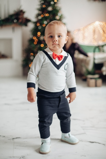 Retrato de corpo inteiro de uma criança na moda com laço vermelho em pé na sala decorada para o Natal