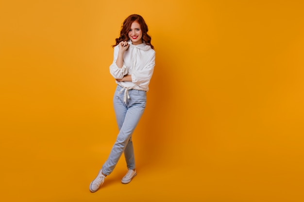 Retrato de corpo inteiro de uma garota atraente com cabelo ruivo. Foto interna da senhora feliz usa jeans e blusa branca.