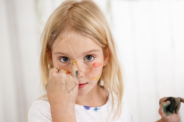 Retrato de criança angelical com manchas coloridas de tinta no rosto