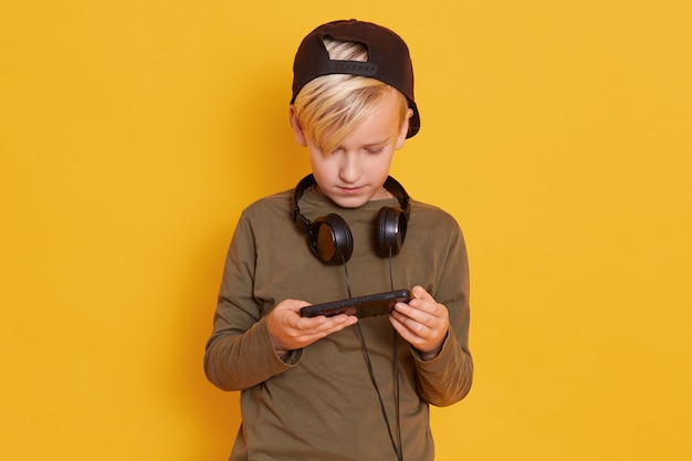 Retrato de criança loira jogando videogame e segurando o smartphone nas mãos