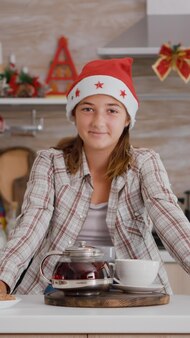 Retrato de criança olhando para a câmera em pé à mesa com biscoitos assados e chá com infusão na cozinha culinária de decoração de natal. neto feliz curtindo as férias de natal