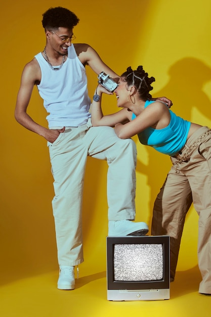 Retrato de dois amigos no estilo de moda dos anos 2000 posando junto com tv e câmera