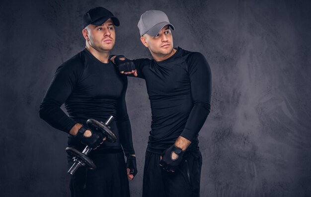 Retrato de dois bonito jovem macho vestido com um sportswear preto e boné de beisebol sobre um fundo escuro.