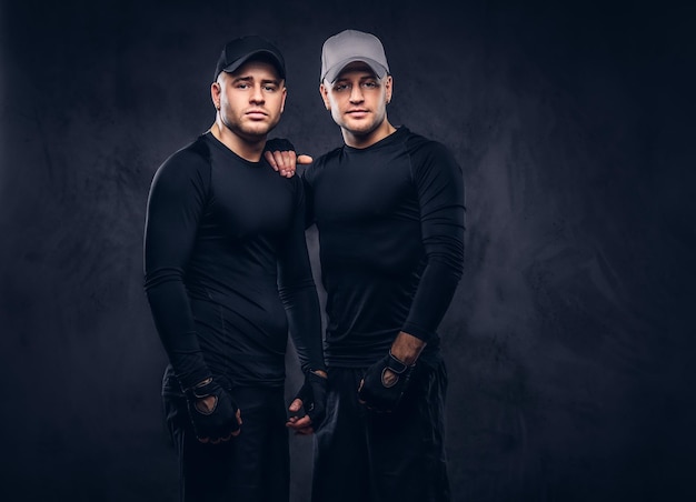 Retrato de dois bonito jovem macho vestido com um sportswear preto e boné de beisebol sobre um fundo escuro.