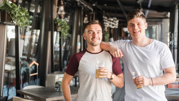 Retrato, de, dois, jovem, macho, amigos, segurando, copos cerveja